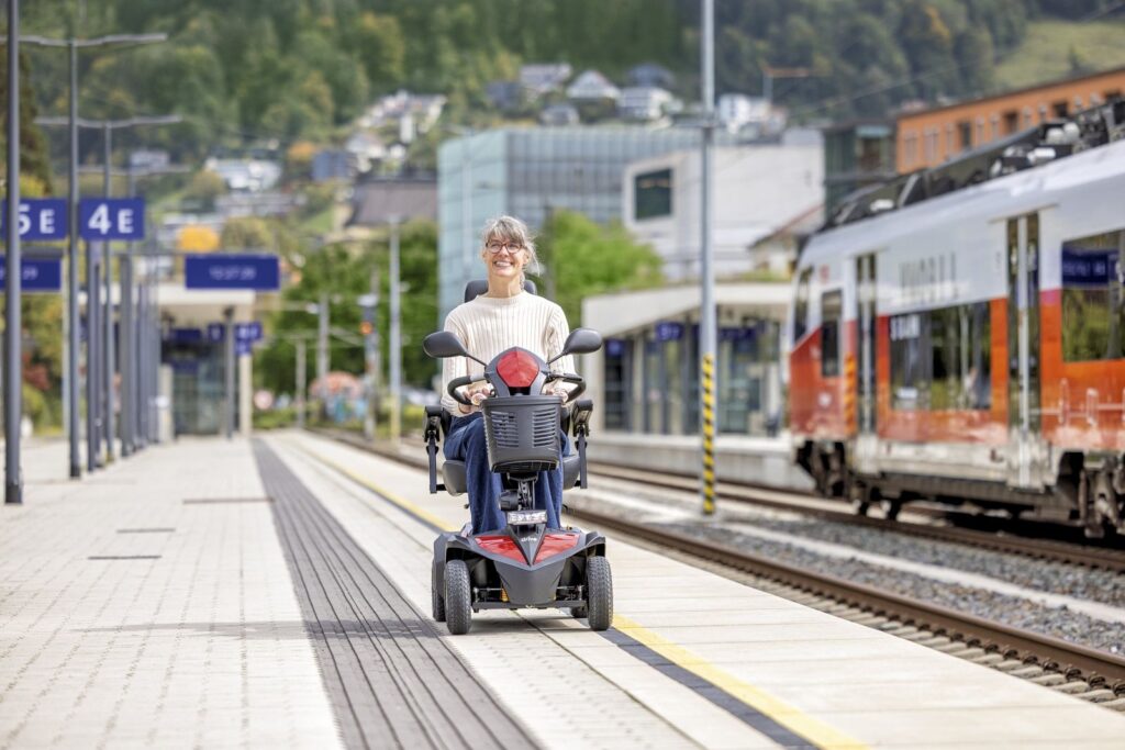 Frau mit einem Elektromobil auf einem Bahnsteig